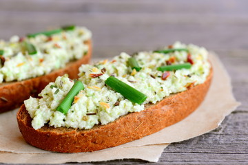 Avocado guacamole toast on a paper and a vintage wooden table. Rye toast with sauce guacamole, fresh green onion and dried herbs. Healthy breakfast. Closeup