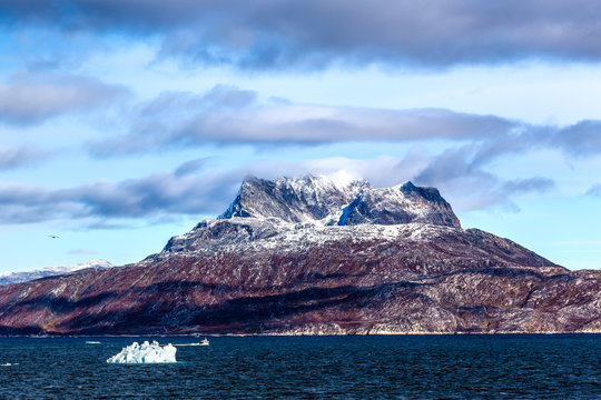 Clouds over Sermitsiaq mountain peaks covered in snow with blue sea in the foreground, nearby Nuuk city, Greenland