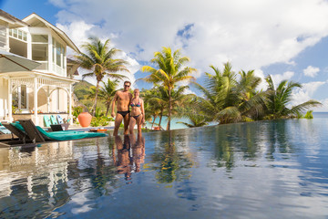 Newlyweds on honeymoon vacations on Mahe island, Seychelles. Couple relaxing by luxury hotel swimming pool surrounded by various type of palm trees on the beach.