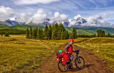in the background snow-white peaks. The photo was taken during a cycling trip through the Altai in the summer in August. Russia. Cyclist woman, girl standing and looking at the mountains, closeup.