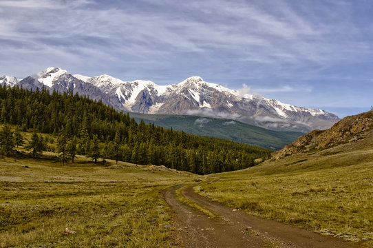 Altai mountain road dirt. in the background snow-white peaks. The photo was taken during a cycling trip through the Altai in the summer in August. Russia.