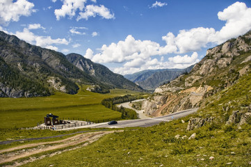 Fototapeta na wymiar Chuiski road, Altai Republic. The road in the mountains, highway, paved road near the shore of the river Chuya. Sunny day in summer. Biking. Grass, herbs around.