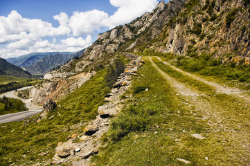 Fototapeta premium Chuiski road, Altai Republic. The road in the mountains, highway, paved road near the shore of the river Chuya. Sunny day in summer. Biking. Grass, herbs around.