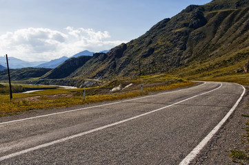 Naklejka premium Chuiski road, Altai Republic. The road in the mountains, highway, paved road near the shore of the river Chuya. Sunny day in summer. Biking. Grass, herbs around.