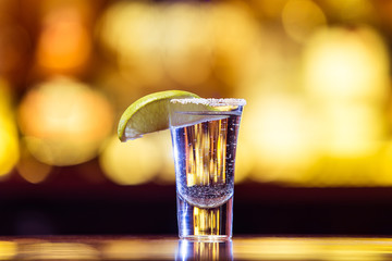One Silver tequila in a glass on a background of bright lights. Traditional Mexican drink.