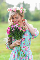 Beautiful blonde girl holding bouquet of flowers at the countryside