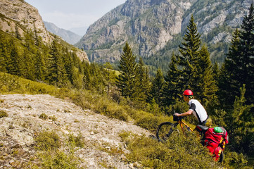 Fototapeta premium Biking on the Altai Republic. Beautiful mountain scenery, forest, green, mountains. A man on a bicycle with a backpack on a slope, trail, mountain road. Sprtivny campaign. Russia. Tourism.