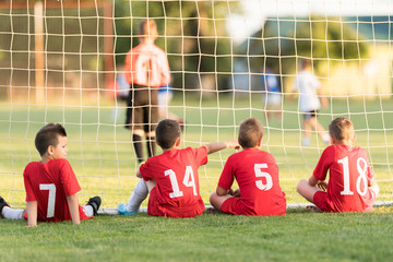 Kids soccer players sitting behind goal watching football match