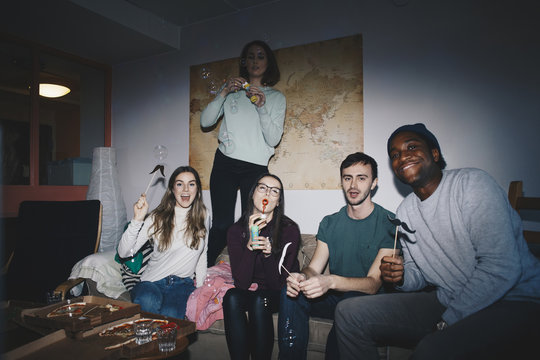 Portrait of cheerful young friends on sofa against world map at college dorm