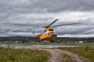 Yellow helicopter comes in to land, an abandoned area around the old village, river, forest. Helicopter close-up.