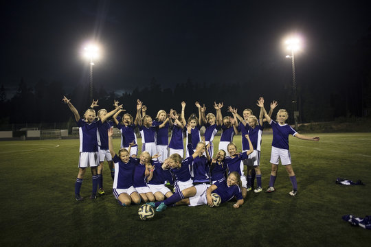 Portrait of cheerful girl's soccer team on illuminated field against sky