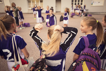 Rear view of girl tying ponytail standing amidst friends on footpath