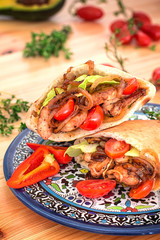 Stuffed pita bread with fried chicken with onions, lettuce leaves, cherry tomatoes and poured sauce on a traditional painted plate. Wooden background. Top view. Close-up