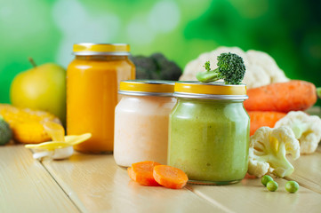 Jars with vegetable puree on the light wooden background