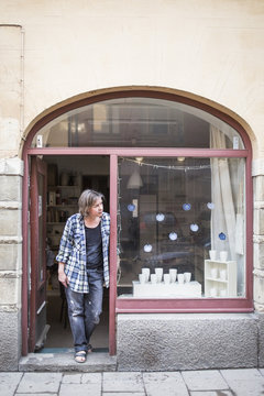 Mature female ceramic store owner standing at doorway while looking away