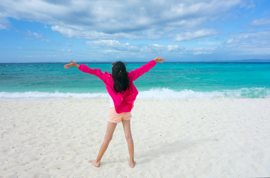 Joyful Young Asian pre teen girl in pink jacket holding hands and breathing fresh air standing on white sand beach with clear blue sea. Summer outdoor holiday serenity. Kalanggaman Island, Philippines