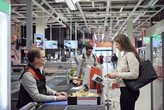 Mature cashier looking at woman paying through technology at checkout counter in supermarket