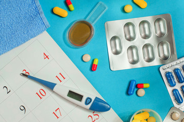 Pills, spoon of syrup, electronic thermometer near calendar page