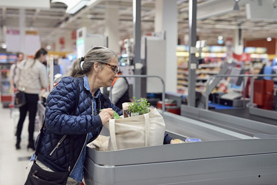 Mature woman putting groceries at checkout counter in supermarket