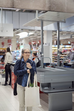 Mature woman carrying shopping bag while walking against checkout counter at supermarket