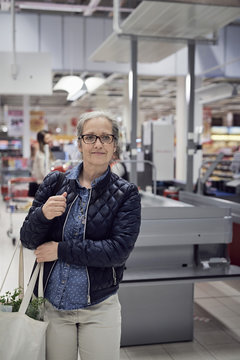 Smiling mature woman carrying shopping bag while looking away against checkout at supermarket