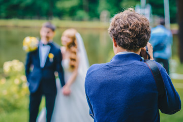 A wedding photographer takes pictures of the bride and groom in nature, the photographer in action - 158974018