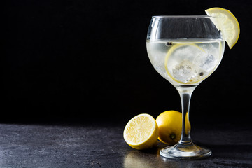 Glass of gin tonic with lemon on black stone background
 - obrazy, fototapety, plakaty