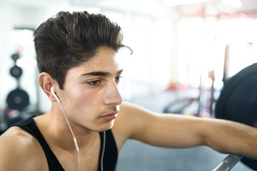 Hispanic man in gym resting, earphones in his ears,listening mus