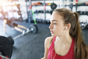 Fototapeta premium Young woman in gym, earphones in her ears,listening music