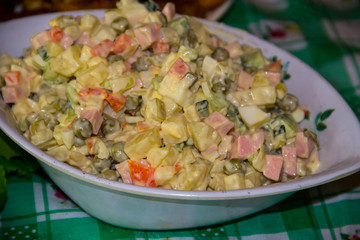 Russian traditional salad olivier with green pea, eggs, pickled cucumber, potato, sausages and mayonnaise