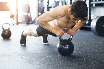 Young fit hispanic man in gym doing push ups on kettlebell.