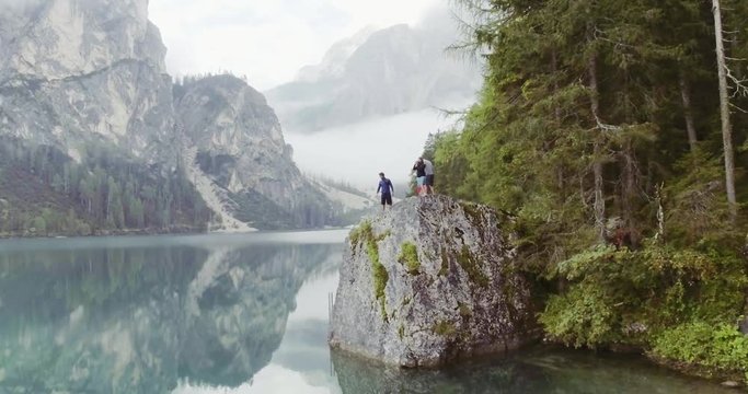 Aerial drone flight over group of friends people looking at lake.Summer adventure journey in mountain nature outdoors. Travel exploring Alps, Dolomites, Braies, Italy. 4k video forward