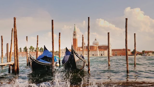 Two gondolas at the pier against the backdrop of the coastline of Venice, Italy. In the foreground, water splashes, slow motion 4K video