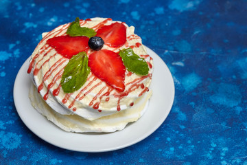 White creamy round cake with strawberries and mint on plate