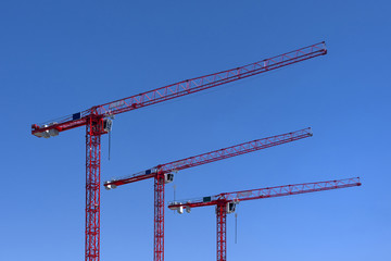 Three red industrial construction tower cranes against blue sky