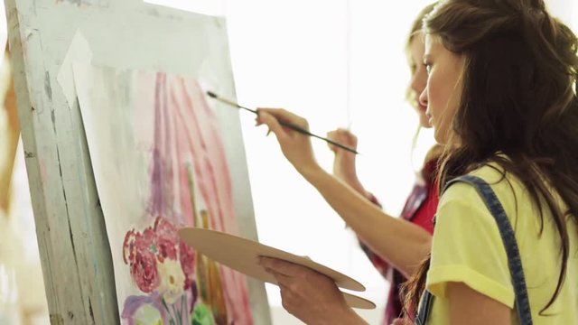 student girls with easel painting at art school