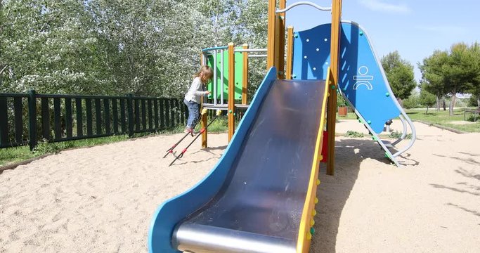 Three years old blonde child playing sliding in metal slide in outdoor playground, in public Park Valdebebas, Madrid Spain
