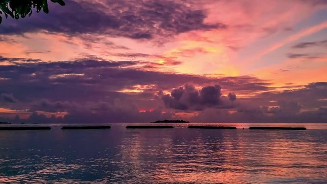 Timelapse of colorful sunset on island in Maldives with orange sky, dark clouds and island at horizon. The sun sets over the horizon. Absence of people