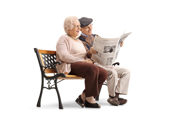 Joyful senior couple sitting on bench and reading newspaper together