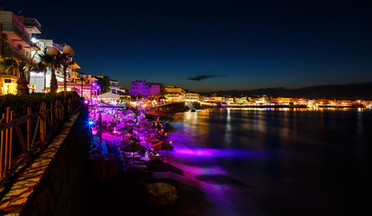 Fototapeta premium Beautiful evening with night shore with a beach and umbrellas and highlighted with bright colorsin Hersonissos bay Crete, Greece 