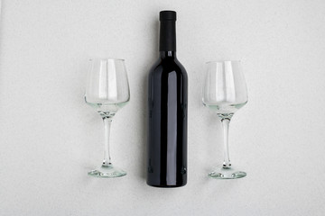 Overhead angled view of a large bottle of red wine, drinking glasses on white background