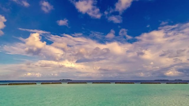 Timelapse of early morning on island in Maldives with blue sky, white clouds, turquoise water and island at horizon. Moving clouds. Absence of people