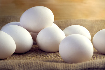 White chicken eggs wrapped in burlap next to a basket on a wooden table