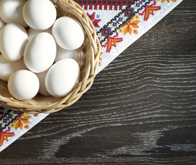 White chicken eggs wrapped in burlap next to a basket on a wooden table