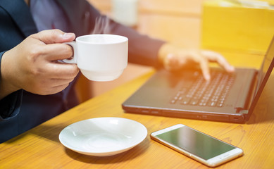 A young business man holding cup of coffee and use a laptop in the office on blur background.