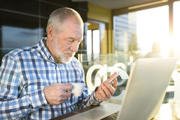 Senior businessman with smartphone and laptop in cafe