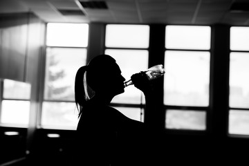 Resting time. Silhouette of sporty girl drink water. Photo of fitness model. Health concept.