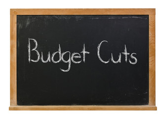 Obraz premium Budget Cuts written in white chalk on a black chalkboard isolated on white