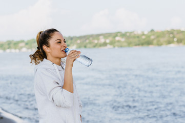 Girl drinking water after workout by the river side.