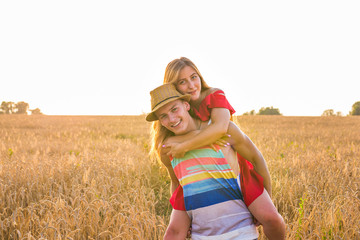 Happy Couple Having Fun Outdoors on wheat field over sunset. Laughing Joyful Family together. Freedom Concept. Piggyback.